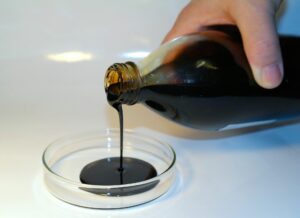 Eine Flasche voller Öl, die von einer Hand in eine kleine durchsichtige Schüssel geschüttet wird